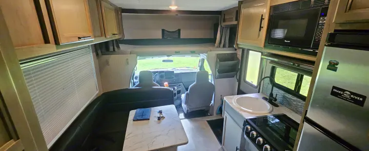 RV rental interior showing a dinette, kitchen with stove/sink/microwave, cab seats, and overhead bunk.. Coachmen Cross Trail 2023