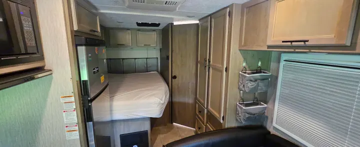 This rv rental interior showcases a compact bedroom area with a bed, kitchen appliances, and integrated storage solutions.. Coachmen Cross Trail 2023