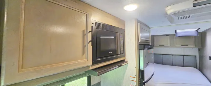 This RV rental features a kitchenette with a microwave and fridge, extending to a bedroom with a comfortable bed. AC unit overhead.. Coachmen Cross Trail 2023