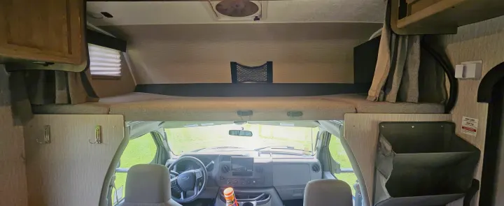 RV rental interior: forward view of the driver's cockpit with a steering wheel, an overhead bunk bed, and various storage solutions.. Coachmen Cross Trail 2023