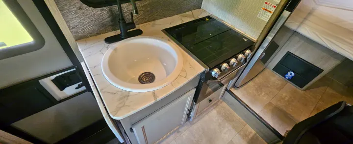RV rental kitchen featuring a white sink, black faucet, and a stove/oven combo on a marble-patterned countertop.. Coachmen Cross Trail 2023