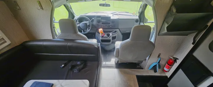 Experience this rv rental interior: cockpit, front seats, dining area with a black couch & table, plus a fire extinguisher for safety.. Coachmen Cross Trail 2023