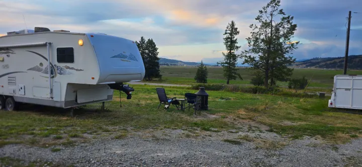 RV rental parked in a scenic field with outdoor chairs and a fire pit, offering a tranquil view of distant mountains.. R-Vision Trail-Lite Trail-Bay 2005