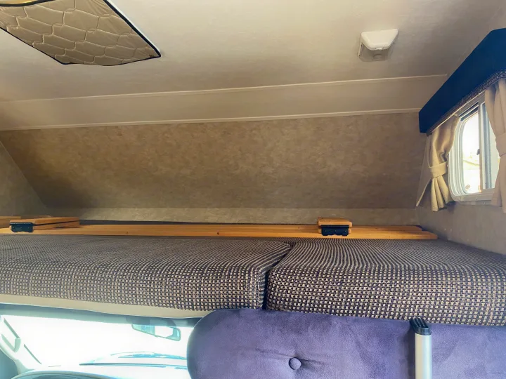 Interior view of an RV rental's cab-over bunk, featuring a bed, wooden slats, a window, and ceiling light.. Adventurer Adventurer Motorhome 2008