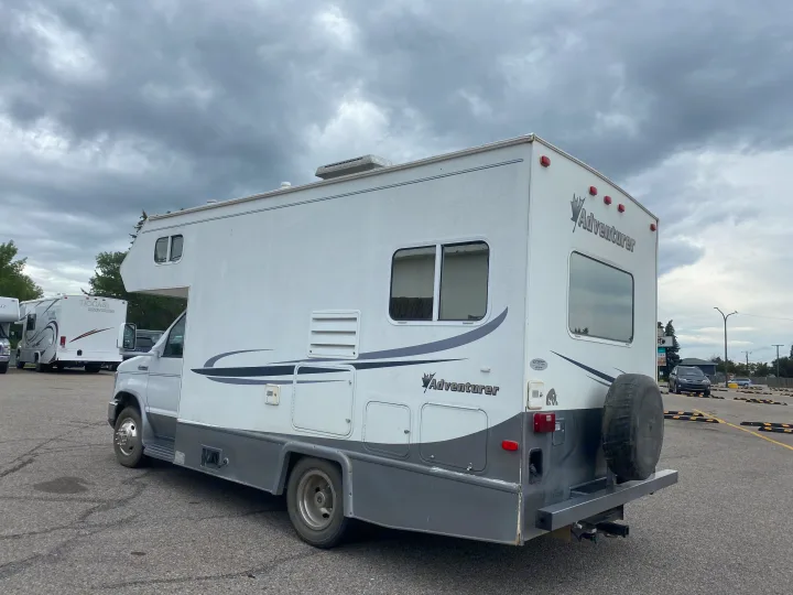 A white Adventurer RV rental is parked in a lot under overcast skies, seen from its rear side with a spare tire.. Adventurer Adventurer Motorhome 2008