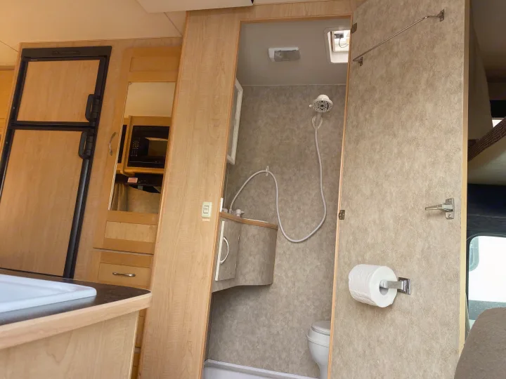 View inside an RV rental showing a compact kitchen with refrigerator, microwave, sink, and a full bathroom with toilet and shower.. Adventurer Adventurer Motorhome 2008