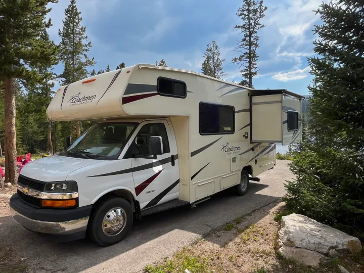 Spacious RV rental parked among pine trees with a lake view, perfect for outdoor adventures.. Coach House Freelander 2017