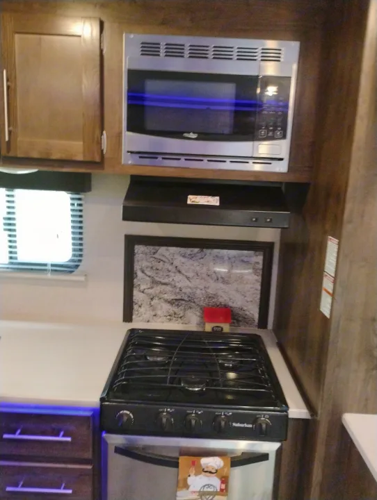 Inside an RV rental: a compact kitchen featuring a microwave, Suburban stovetop/oven, and blue-lit cabinets.. Crossroads RV Volante 2019