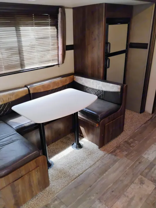 Inside an RV rental: a comfortable dinette area with U-shaped seating, a white table, and window blinds.. Crossroads RV Volante 2019
