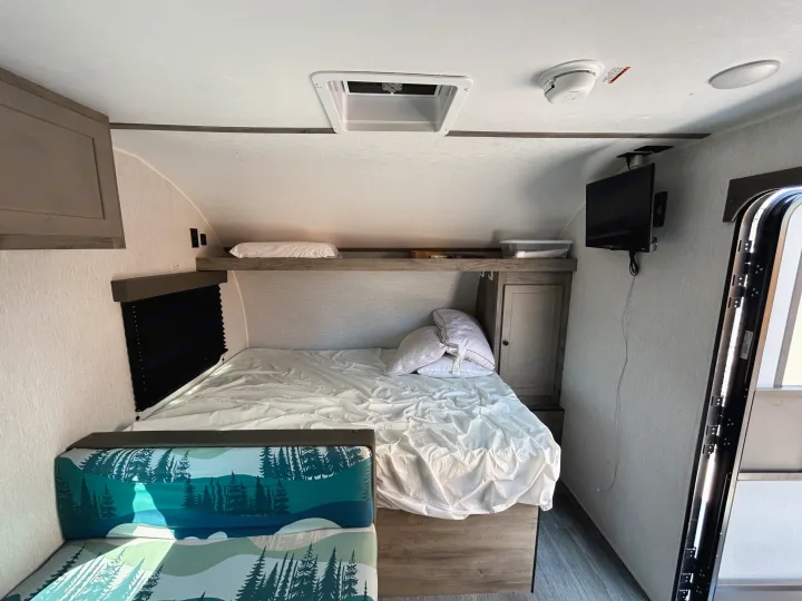 Explore this rv rental's interior: a comfortable bed, forest-patterned bench, TV, and convenient overhead storage.. Sunset Park & Rv Inc. 21bt 2026