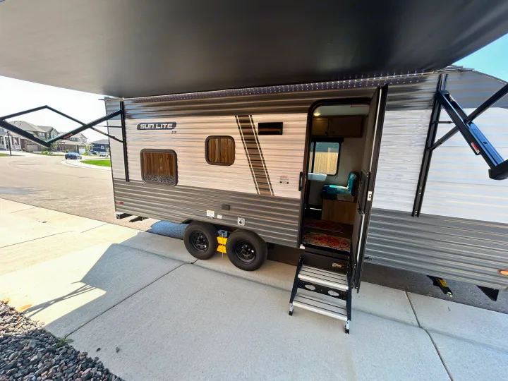 An RV rental travel trailer, a Sun Lite LTD, parked with its awning extended and door open, revealing the interior.. Sunset Park & Rv Inc. 21bt 2026