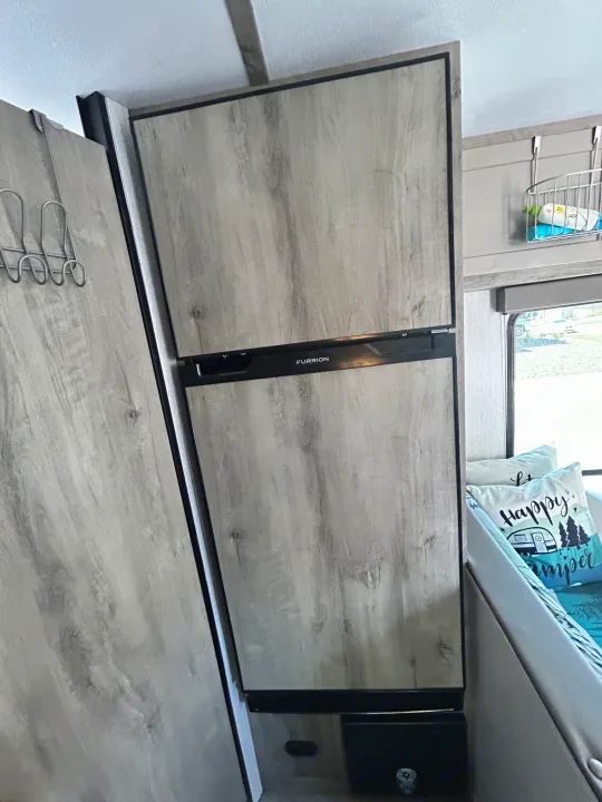 Modern RV rental interior with a built-in Furrion refrigerator, storage cabinet on left, and a dinette to the right.. Sunset Park & Rv Inc. 21bt 2026