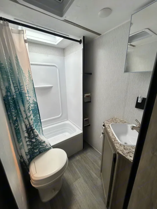 See this RV rental's compact bathroom with a shower/tub, toilet, and vanity sink, featuring a forest-themed curtain.. Sunset Park & Rv Inc. 21bt 2026
