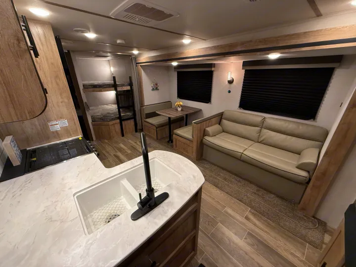 Modern RV rental interior featuring a bright kitchen, cozy dinette, comfortable sofa, and convenient bunk beds.. Gulf Stream Ameri-Lite 2023