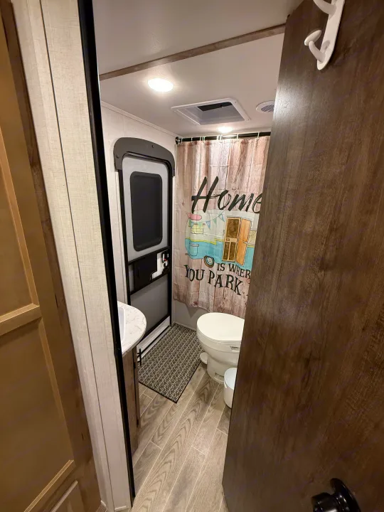 RV rental bathroom featuring a toilet, vanity, and a rustic "Home is where you park it" shower curtain.. Gulf Stream Ameri-Lite 2023