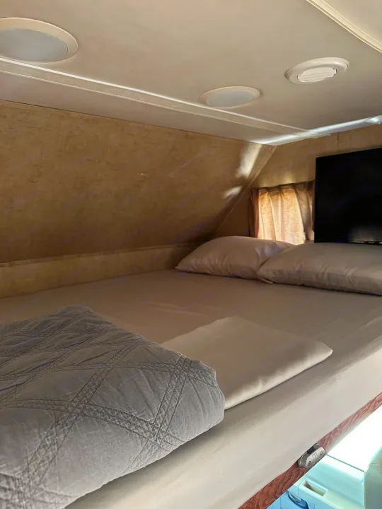 An inviting RV rental sleeping area: a neat bed with fresh linens, pillows, gray quilted blanket. Ceiling lights, vent, and TV are visible.. Forest River Forester 2861DS 2016