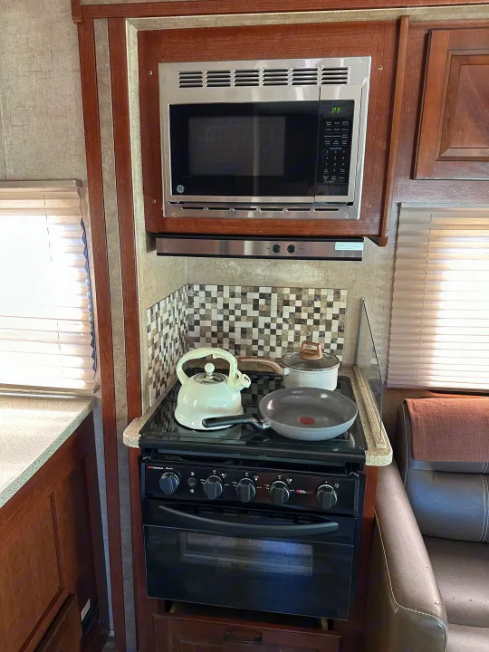 RV rental kitchen with a black Suburban stove/oven, GE microwave, and white teapot on the cooktop. Ready for meals on the go.. Forest River Forester 2861DS 2016
