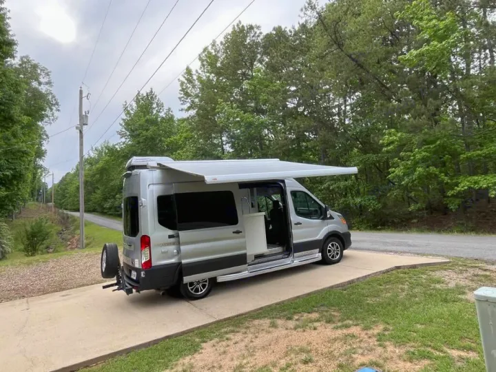 Silver camper van with extended awning & open door, ready for your trip. Book this comfortable rv rental for outdoor adventures!. Pleasure-Way Pleasure-Way Class B 2023
