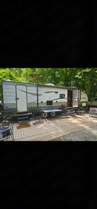**RV rental** at a peaceful campground, showcasing outdoor living space with a rug, chairs, and table. Perfect for relaxation!. Forest River Cherokee Grey Wolf 2016