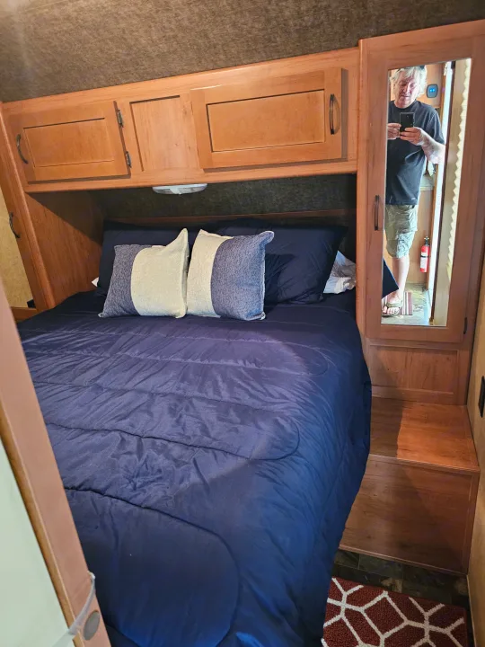 Cozy RV rental bedroom with dark blue bedding, overhead cabinets, and a reflective mirror showing the photographer.. Forest River Cherokee Grey Wolf 2016