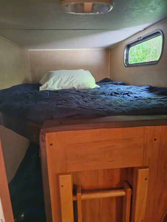Cozy RV rental sleeping area with a bed, blue comforter, white pillow, overhead light, and window.. Forest River Cherokee Grey Wolf 2016