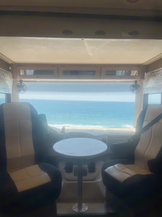 RV rental offers stunning ocean view from inside; features front seats, table, and beach scene.. Thor Windsport 2018