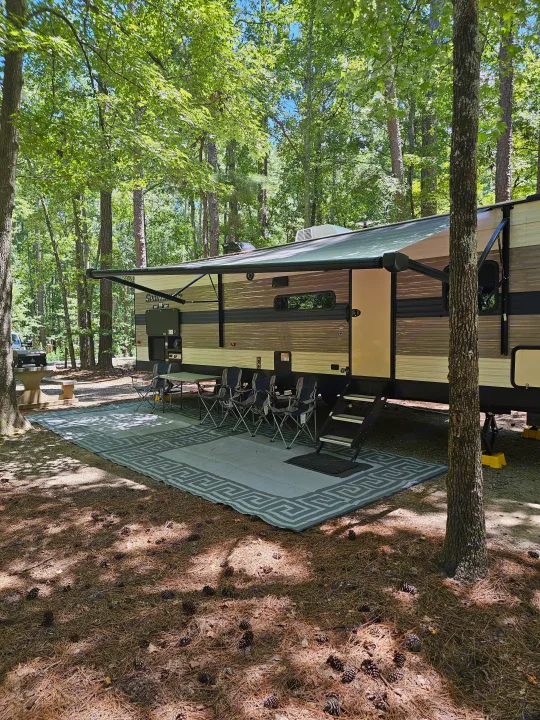 Relaxing RV rental campsite: large trailer with awning, outdoor mat, and chairs under shady trees.. KZ Sportsman 2021