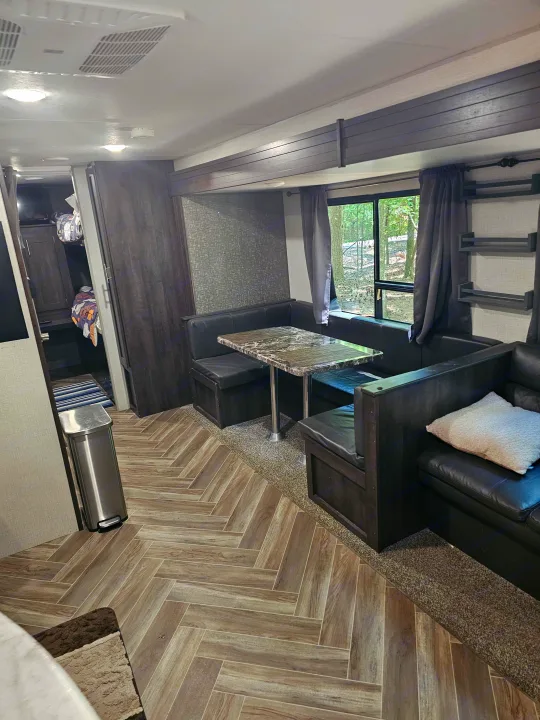 Experience comfort in this RV rental's interior, featuring a dining booth, lounge seating, and stylish wood-look floors.. KZ Sportsman 2021