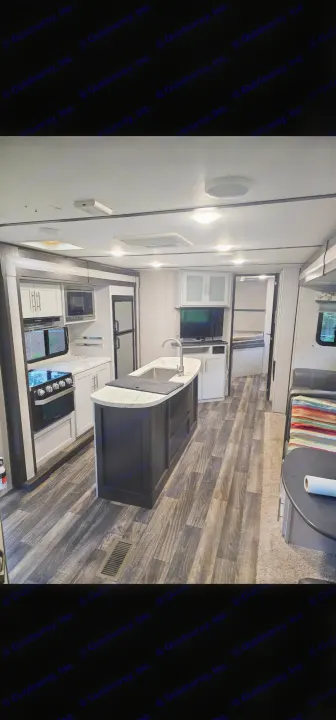 Modern RV rental interior: kitchen with island, stove, & fridge; comfortable living area & bedroom visible. Wood-look flooring.. Keystone RV Bullet Ultra Lite 2019