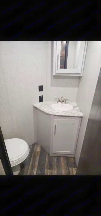 RV rental bathroom interior: showing a corner vanity with sink, mirror, toilet, and wood-look floor.. Keystone RV Bullet Ultra Lite 2019