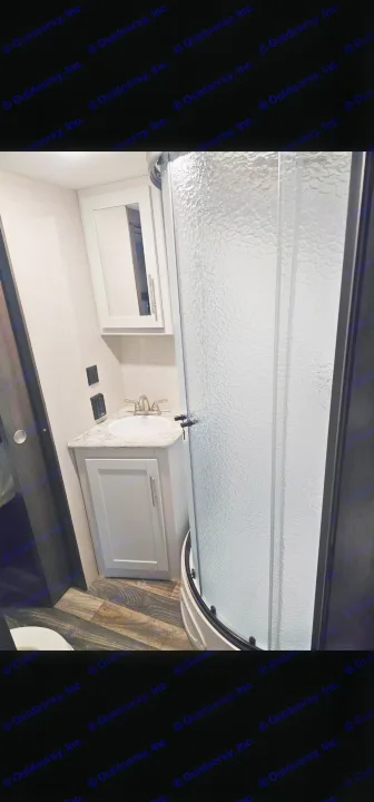 This RV rental bathroom features a compact sink vanity, medicine cabinet, and a curved textured glass shower.. Keystone RV Bullet Ultra Lite 2019