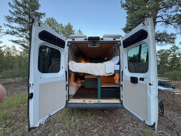 Ultimate RV rental: Customized camper van with open doors, comfy bed, solar panels, and outdoor camping setup.. RAM Promaster 2500 2018