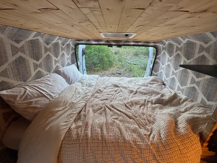 Cozy RV rental interior featuring a comfortable bed, wooden ceiling, patterned walls, and a beautiful nature view.. RAM Promaster 2500 2018
