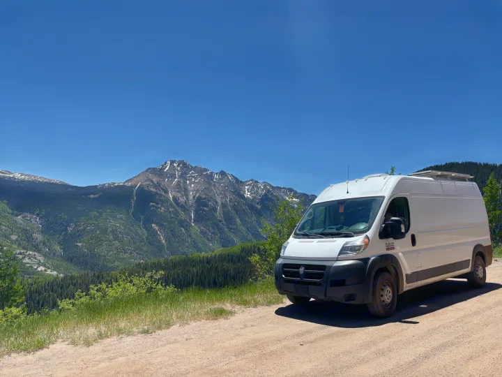 This RV rental, a white camper van, enjoys a scenic mountain view with snow-capped peaks and lush forests.. RAM Promaster 2500 2018