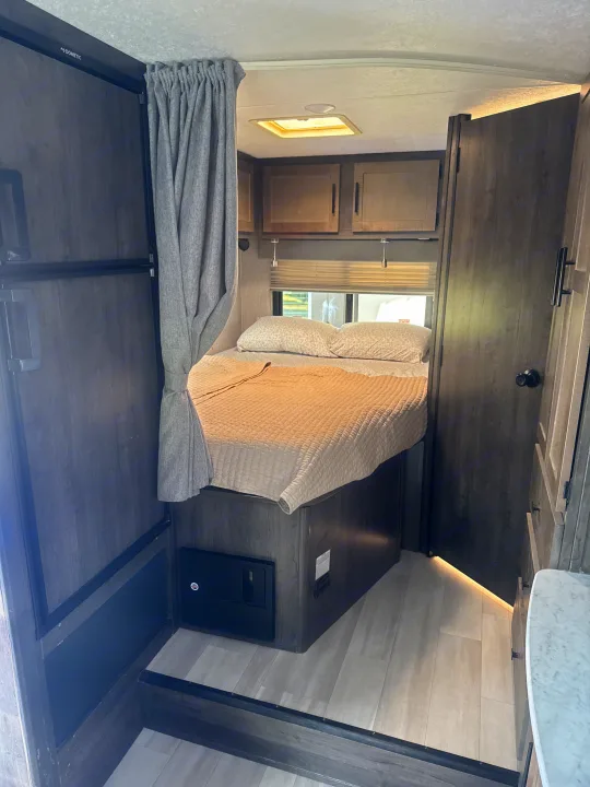 Inside this **RV rental**: a compact bedroom with a cozy bed, overhead storage, and a Dometic fridge for comfortable travel.. Coachmen Leprechaun 23CB 2022