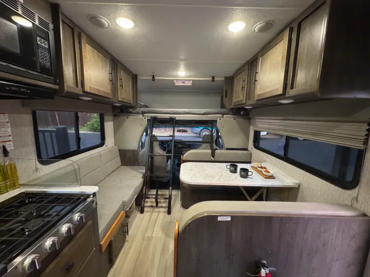 Bright RV rental interior with kitchen, dinette, sofa, and overhead bunk ready for your next adventure.. Coachmen Leprechaun 23CB 2022