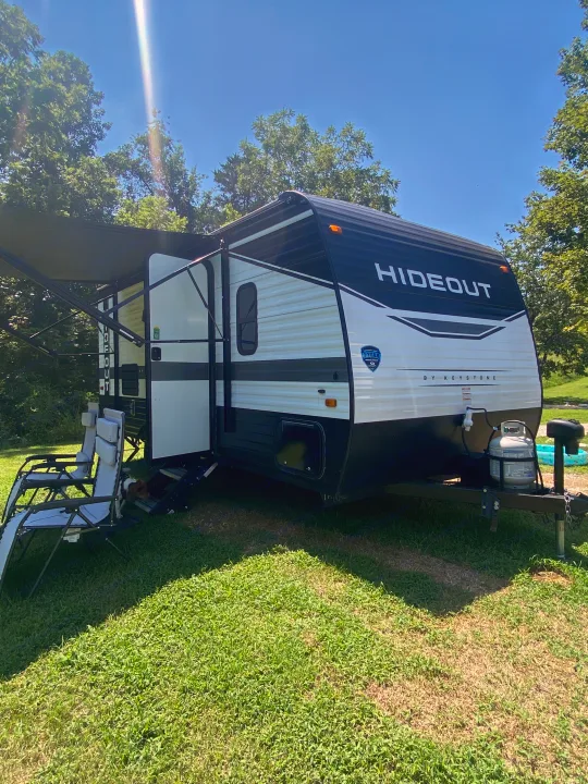 Enjoy your RV rental! A Hideout by Keystone travel trailer is set up at a sunny campsite with an awning, chairs & a dog.. Keystone RV Hideout 2022