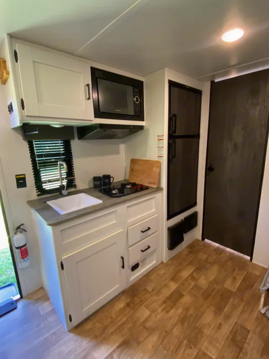 This RV rental offers a modern kitchen setup with white cabinets, microwave, sink, stove, and fridge.. Keystone RV Hideout 2022