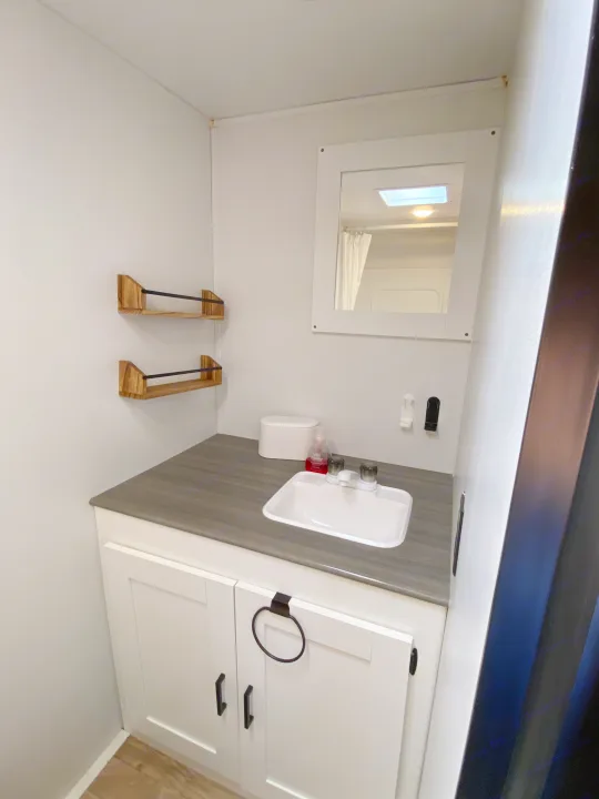Compact RV rental bathroom featuring a modern vanity, sink, mirror reflecting the shower, and wooden wall shelves.. Keystone RV Hideout 2022