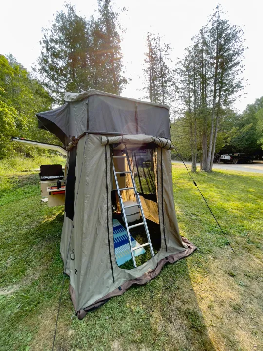 Camping with an overland rooftop tent, part of a unique RV rental experience. Shows a large tent, ladder, and outdoor kitchen.. Nutshell Campers Nutshell Camper 2025