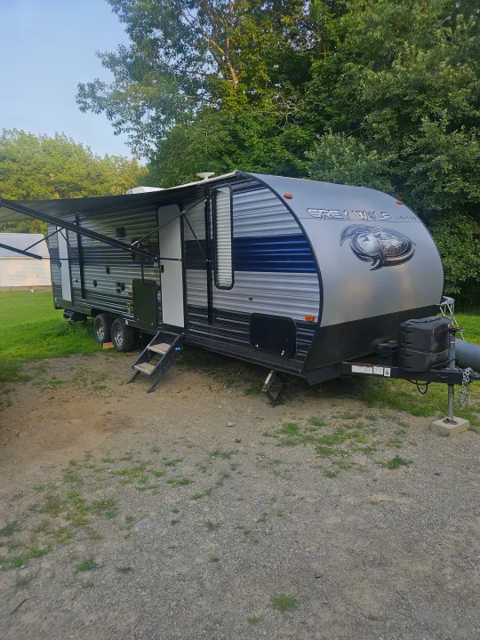 Grey Wolf travel trailer, an excellent rv rental option, parked with awning out on a gravel lot amid green trees.. Forest River Cherokee Grey Wolf 2021
