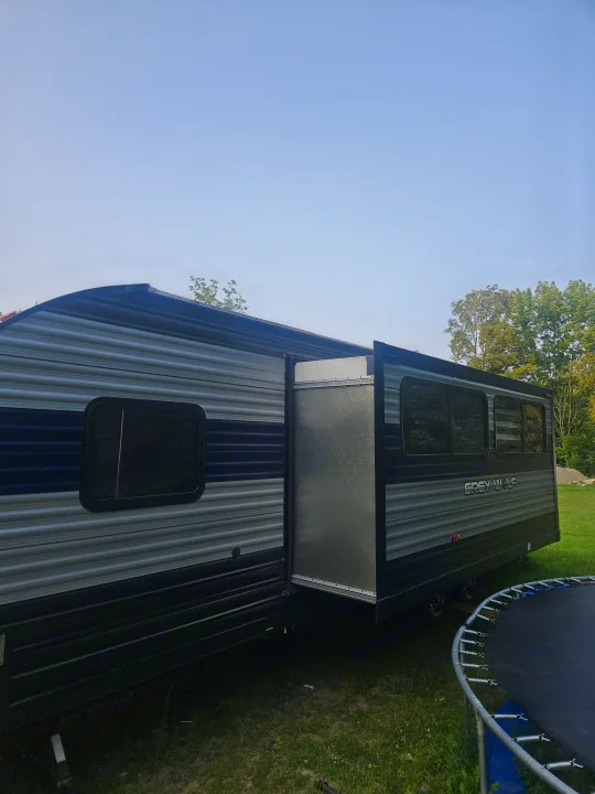 Grey Wolf travel trailer rv rental, with its side slide-out extended, parked on green grass. A trampoline is visible.. Forest River Cherokee Grey Wolf 2021