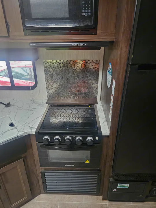 RV rental kitchen with microwave, gas range, sink, and fridge. Compact setup for comfortable travel cooking.. Forest River Cherokee Grey Wolf 2021