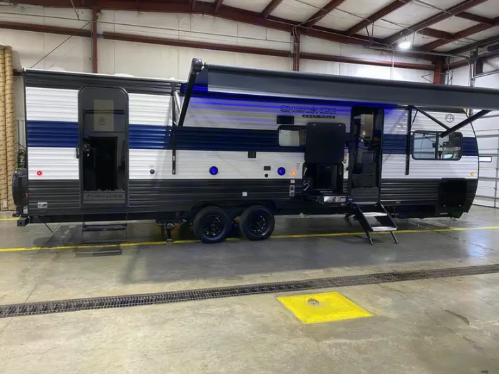 This travel trailer, available for RV rental, features an extended awning, blue lights, and an outdoor kitchen for your adventures.. Grey Wolf 26DBH 2025