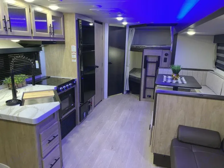 This RV rental interior showcases a kitchen, dinette, and bunk beds, all lit with modern blue accent lighting.. Grey Wolf 26DBH 2025