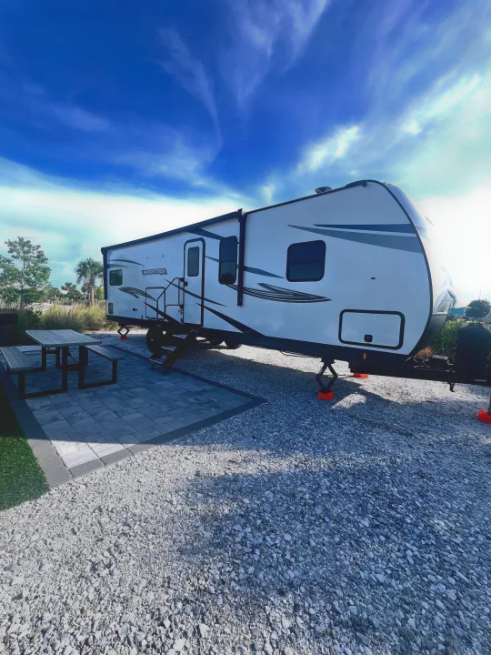 A white Sporttrek RV rental parked at a sunny campsite with a paved patio and picnic table setup, ready for adventure.. SportTrek Venture 2024
