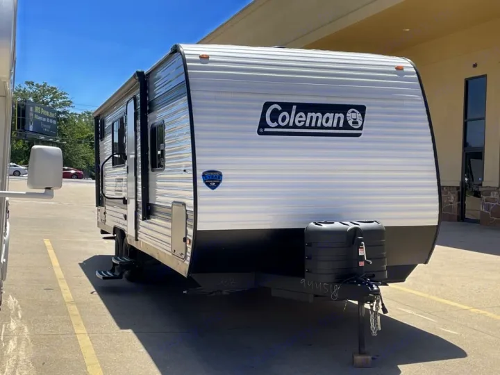 Explore the outdoors! This Coleman travel trailer for rv rental features a sleek white & black design, parked in sunlight.. Coleman 23B Keystone 2025