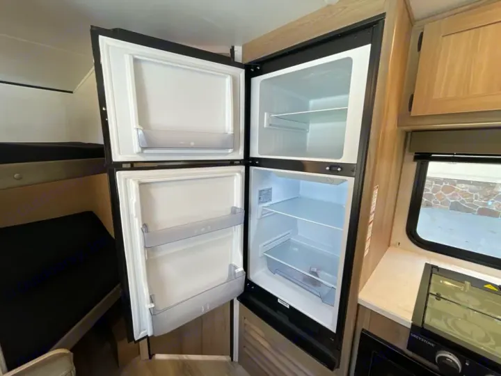 RV rental interior: Open refrigerator, bunk beds, and compact kitchen area. Ready for your adventure!. Coleman 23B Keystone 2025