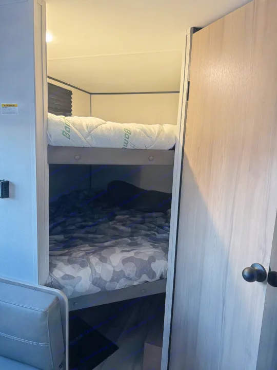 RV rental bunk beds: View of a compact sleeping area with a quilted top mattress and a camo-patterned lower bed.. Colman 23B 2025
