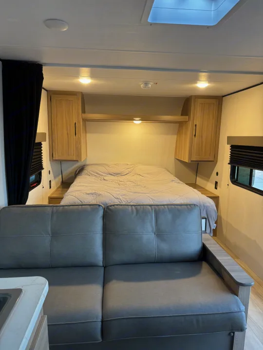 Cozy RV rental interior featuring a comfortable bed, stylish gray couch, wood cabinets, and skylight.. Colman 23B 2025